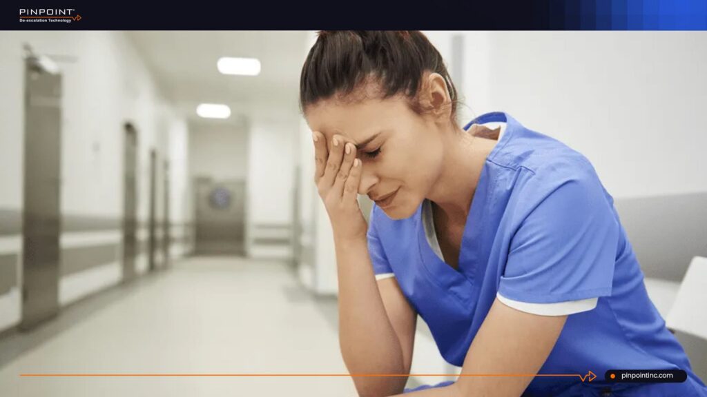 Stressed nurse sitting in hospital hallway showing panic button hesitation in healthcare