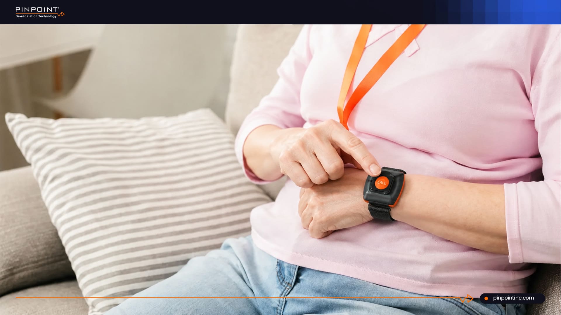 A close-up of a healthcare worker sitting on a couch and pressing a prominent orange "CALL" emergency duress button worn on a black wristband strap.