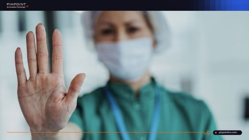 Pinpoint guide on workplace violence prevention in healthcare showing a masked healthcare worker raising a hand to represent staff safety, OSHA compliance, and alert systems.