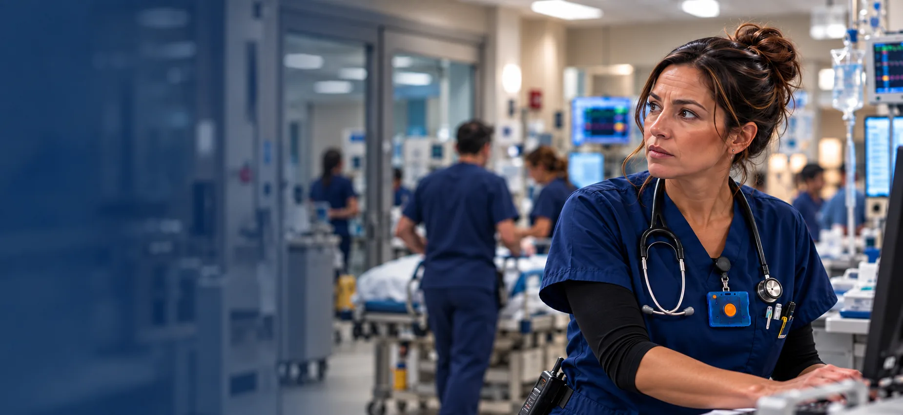 Emergency nurse at a freestanding ED workstation wearing a Pinpoint non-tracking panic button badge on navy scrubs