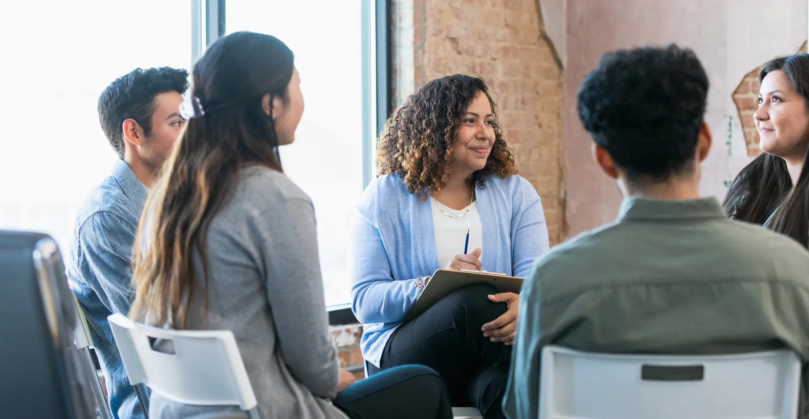 Behavioral health therapist with a clipboard leading a small group therapy session